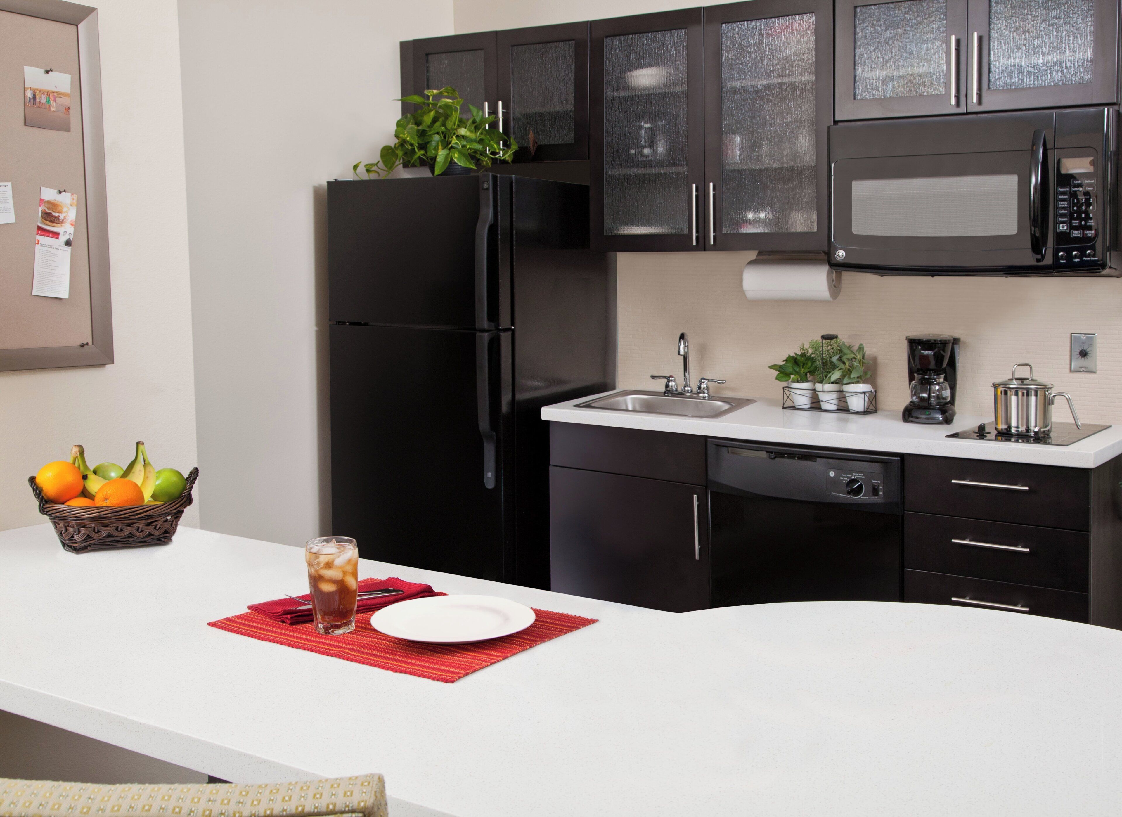 A modern kitchen with a black refrigerator, stainless steel appliances, a white countertop, and a red placemat.