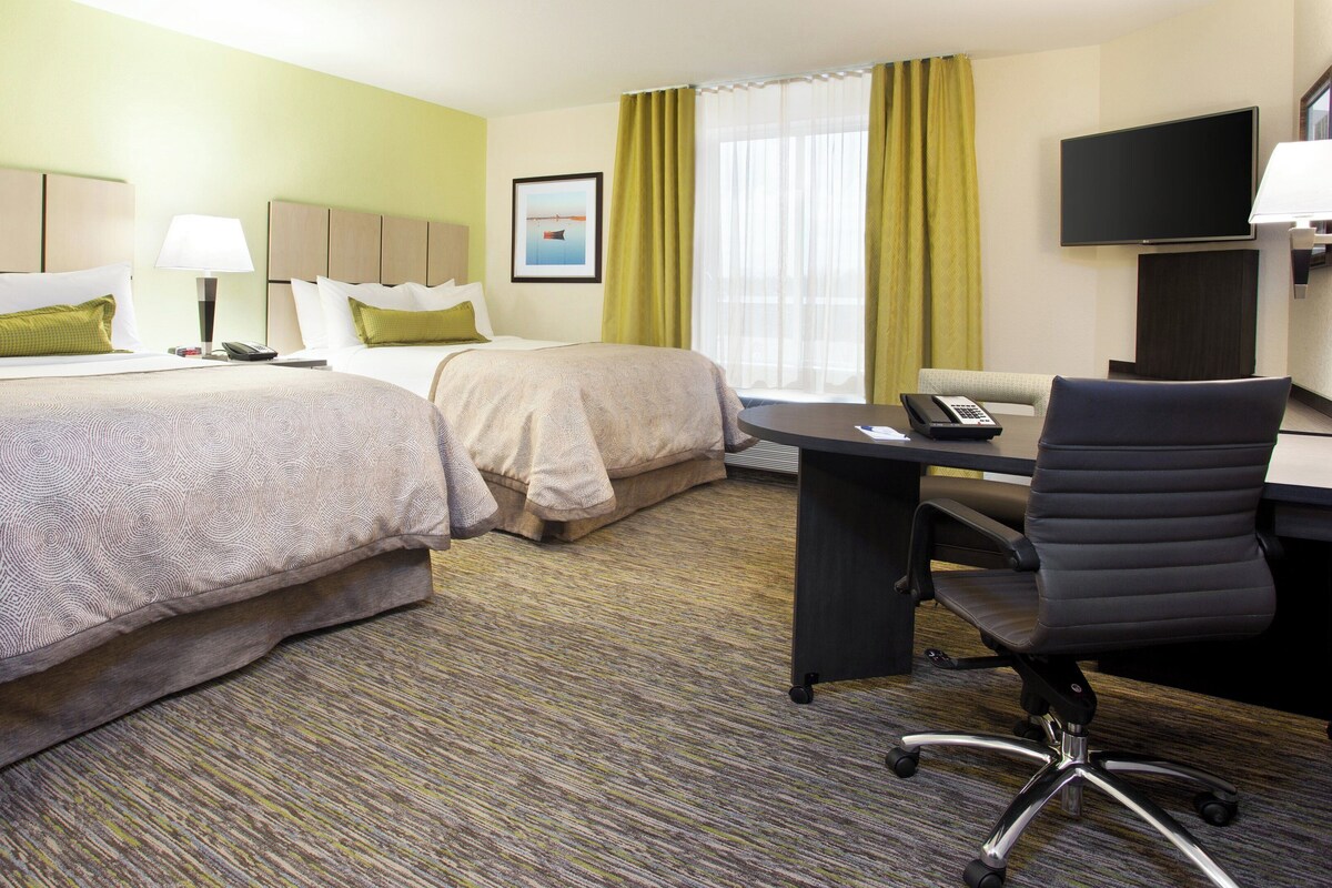 A hotel room with two beds, a desk with a chair, a telephone, and a television.