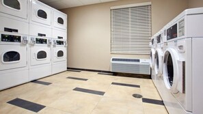 A laundry room with multiple washing machines and dryers, a vented air conditioning unit, and a tiled floor. - Candlewood Suites Carrollton by IHG (Carrollton)