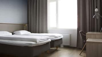 A hotel room with two beds, a desk, and a window with curtains.