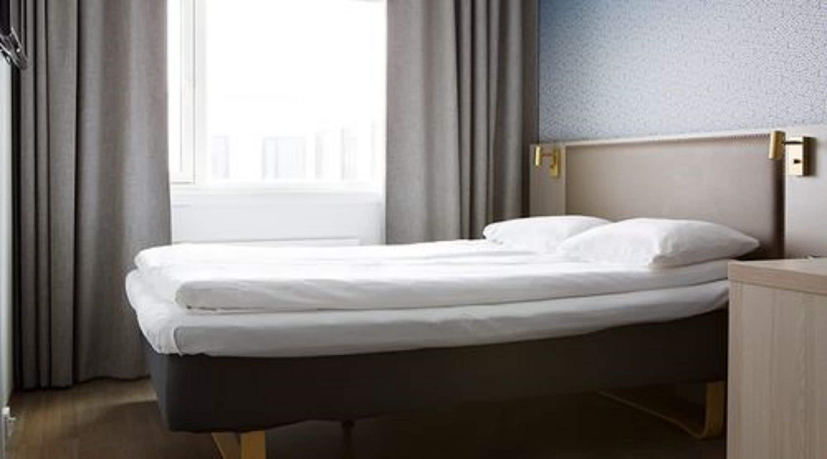 A neatly made bed in a hotel room with a view of the city through the window.