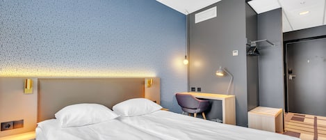 A hotel room with a bed, a desk, a chair, a shower, and a mirror.