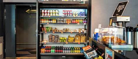 A self-service beverage vending machine stocked with various drinks and snacks, located in a commercial area.
