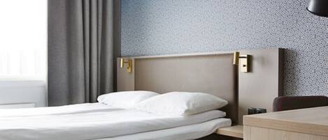 A neatly made bed with white linens, a wooden headboard, and a nightstand with a lamp.