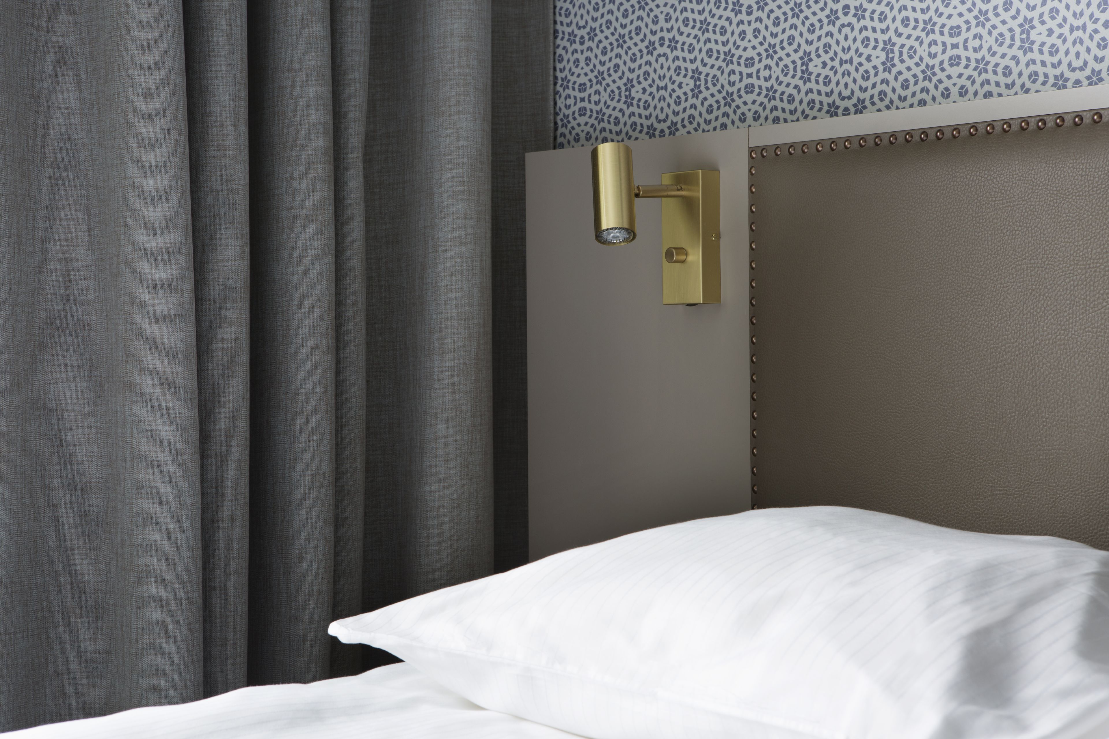 A hotel room with a bed, a wall-mounted light fixture, and a patterned wall.
