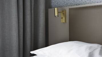 A hotel room with a bed, a wall-mounted light fixture, and a patterned wall.
