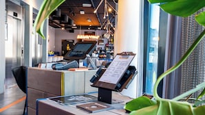 A reception desk with a digital screen, a menu board, and a view of the city through large windows. - Comfort Hotel Xpress Tromso (Tromsø)