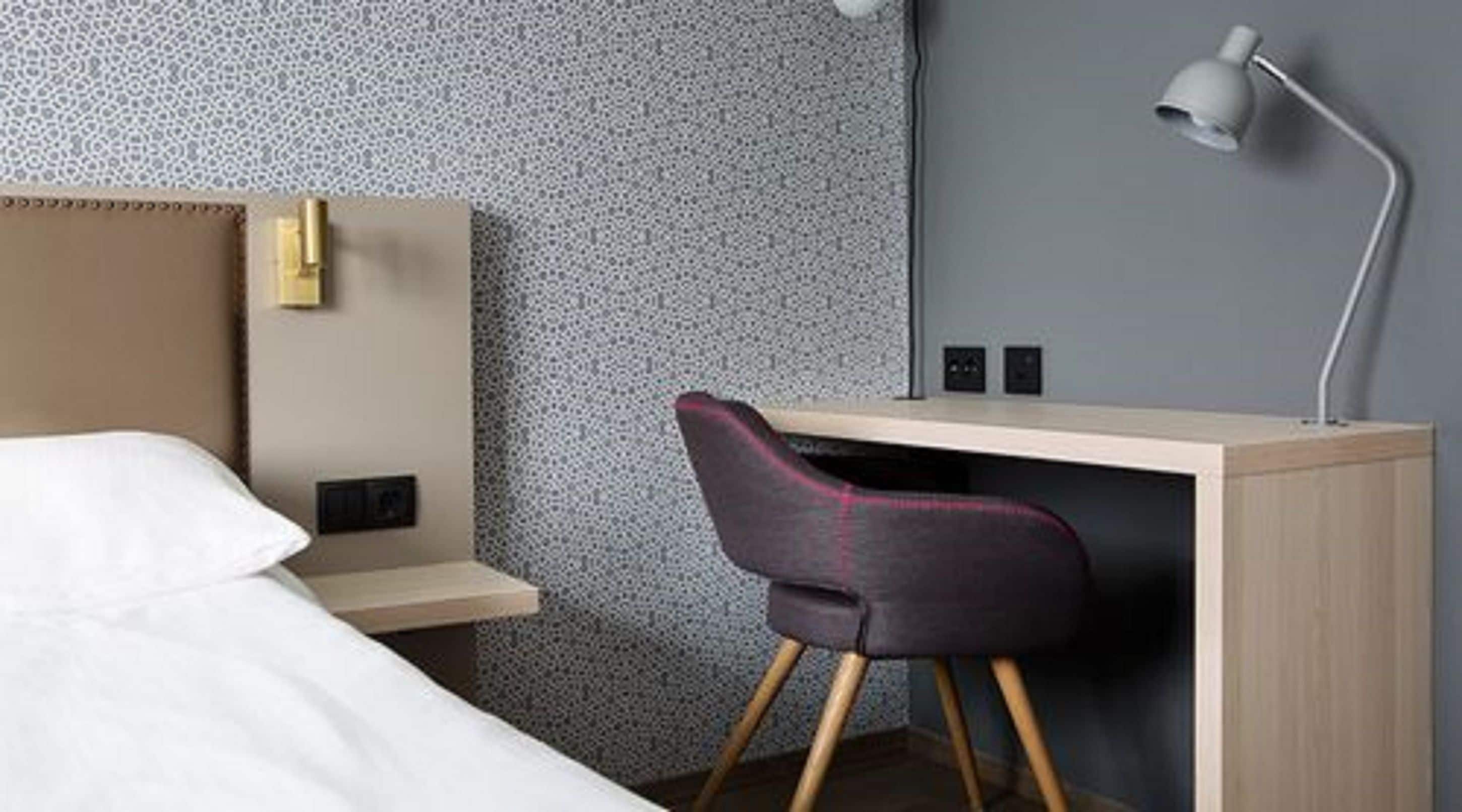Hotelkamer met een bed, een bureau met stoel, een lamp en een kamer met een patroon.