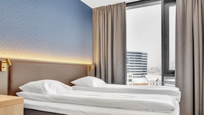 A hotel room with a neatly made bed, a headboard with a textured pattern, a bedside table, and a large window with curtains. - Comfort Hotel Xpress Tromso (Tromsø)