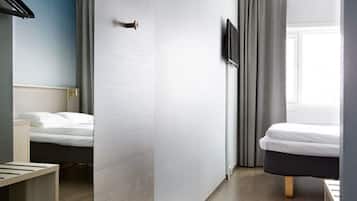 A hotel room with a bed, a bedside table, a TV mounted on the wall, and a window with curtains.
