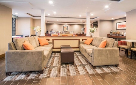 A hotel lobby with a reception desk, two sofas, a coffee station, and a dining area.