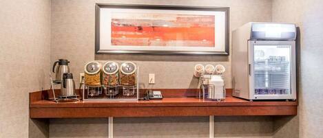 A kitchenette with a coffee machine, a framed abstract painting, and a refrigerator.