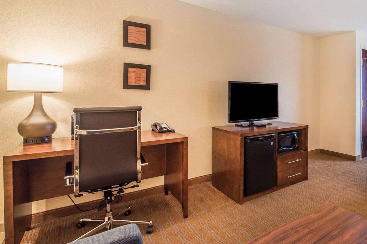 A hotel room with a desk, chair, lamp, television, and a minibar.