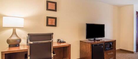 A hotel room with a desk, chair, lamp, television, and a minibar.