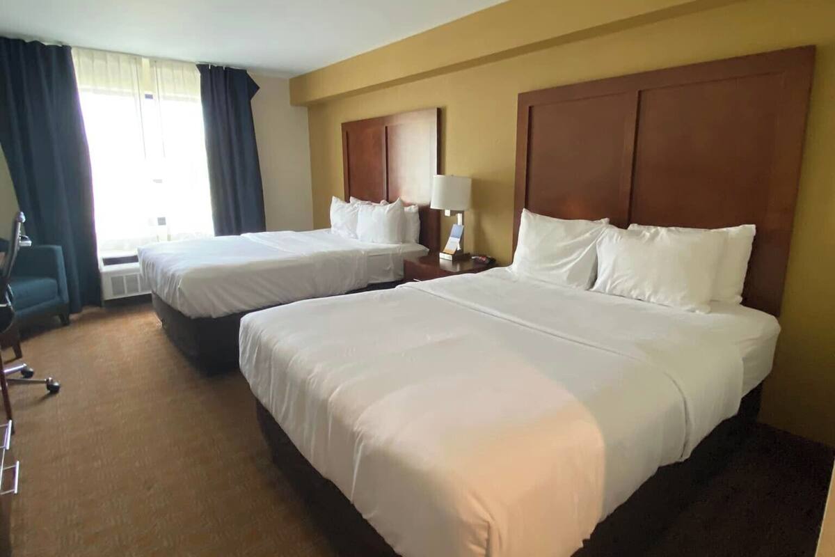 A hotel room with two beds, a desk, and a chair.
