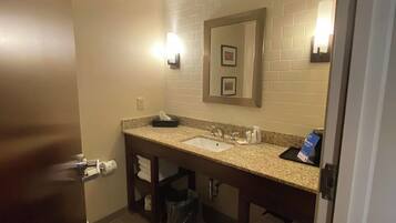 A hotel bathroom with a sink, mirror, towel rack, and trash bin.