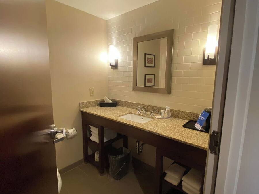A hotel bathroom with a sink, mirror, towel rack, and trash bin.