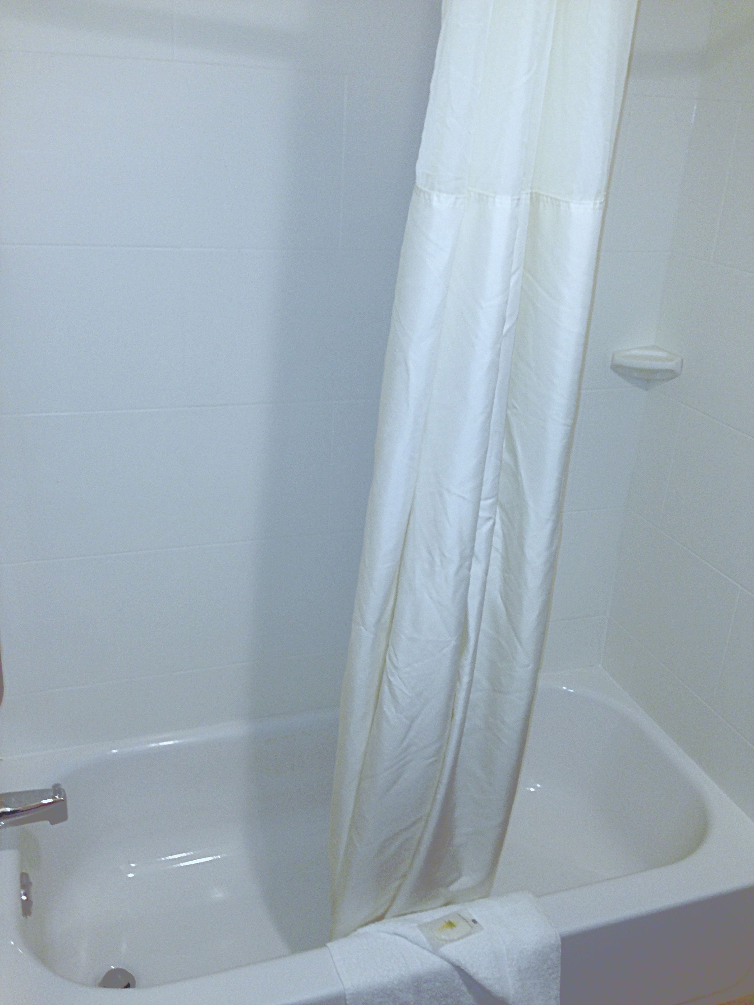 Una bañera blanca con cortina de ducha, una toalla blanca y un jabonera en la pared.