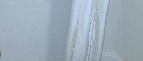 Una bañera blanca con cortina de ducha, una toalla blanca y un jabonera en la pared.
