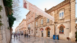 A historic building with a large banner, a tiled pedestrian area, and a storefront with a red 'A' sign. - Marmont City Rooms (Split)