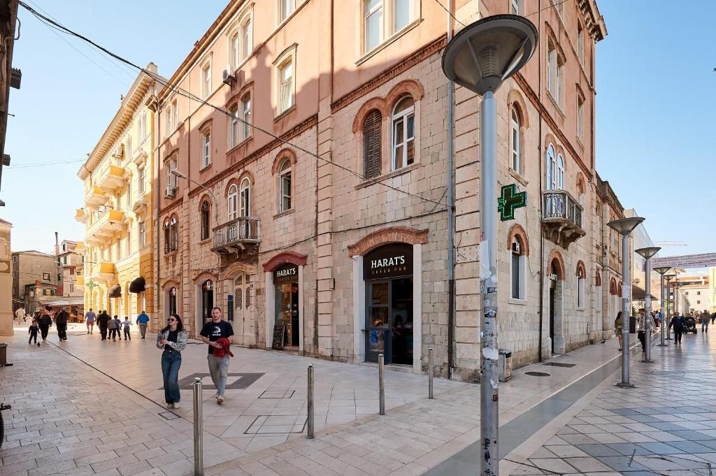 Ruas com edifícios históricos, uma cafeteria Harats e pedestres.