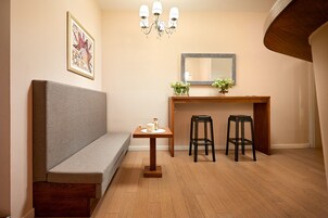 Um quarto pequeno e acolhedor, com um banco, uma mesa de madeira com dois banquinhos, um espelho e um candelabro.