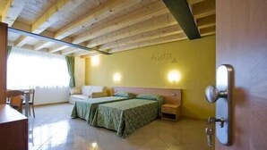 Una habitación con techo de madera, dos camas con ropa de cama verde, una mesita de noche, una lámpara fijada a la pared y una puerta con manija.
