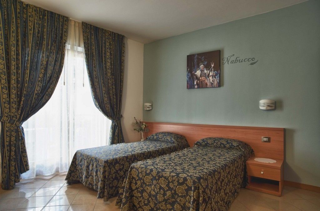 A hotel room with two beds, a wooden headboard, a wall-mounted painting, and a bedside table.