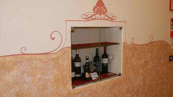 Una dispensa per vino con bottiglie e un bicchiere, su uno sfondo di parete decorata con motivi a spirale.