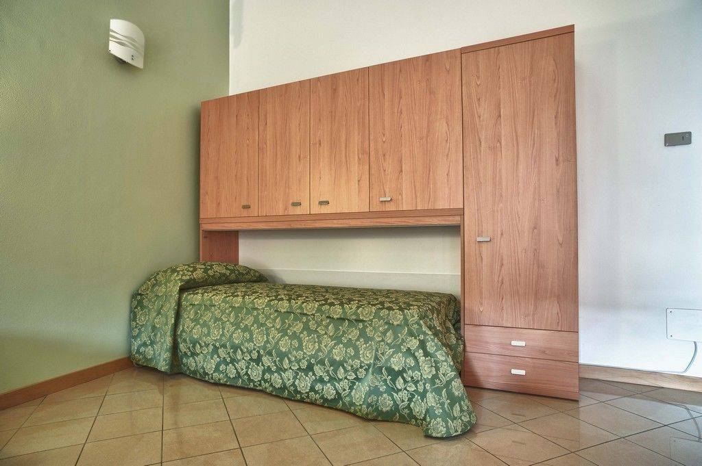 Ein Schlafzimmer mit einem Bett, einem Holzschrank und einer Wandleuchte.