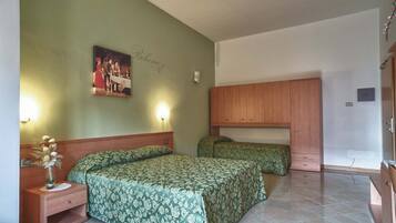 A room with two beds, a wooden wardrobe, a nightstand with a vase, and a wall-mounted light fixture.