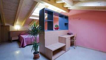 A small, compact room with a sloped ceiling, a built-in wooden desk, a bed with a pink bedspread, and a potted plant.