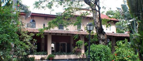 A building with a tiled roof, a covered entrance, and a garden area with potted plants and a pathway.
