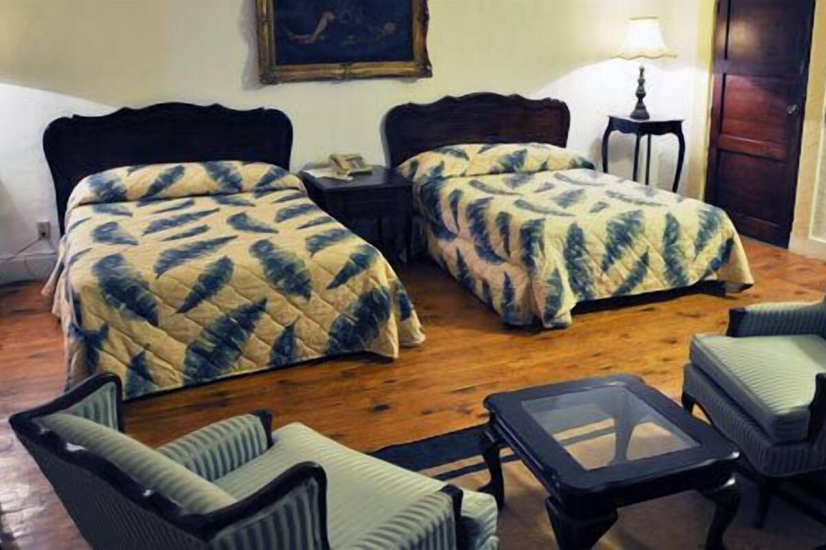 A room with two beds, a small table, two chairs, and a lamp.