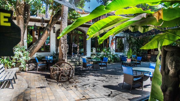 An outdoor patio area with seating, a decorative wheel, and lush greenery. - Hôtel du Roi Christophe (Cap-Haitien)