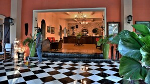 A lobby with a checkered floor, a reception desk, and several potted plants. - Hôtel du Roi Christophe (Cap-Haitien)
