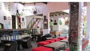 A spacious indoor area with wooden tables and red cushioned seating. There is a staircase leading to an upper level, and a chandelier hangs from the ceiling. - Hôtel du Roi Christophe (Cap-Haitien)