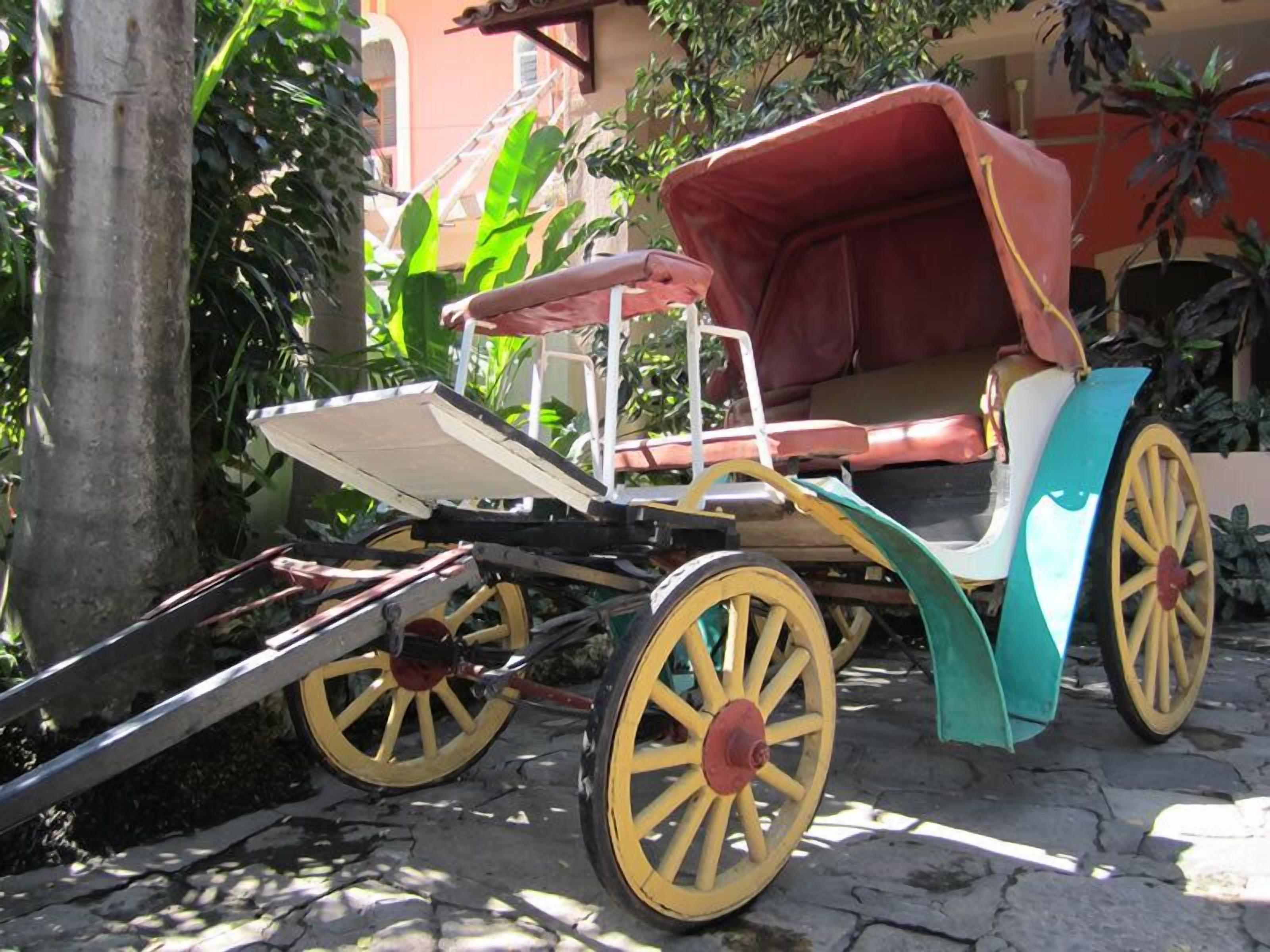 A vintage carriage with a red canopy and yellow wheels parked on a cobblestone path.