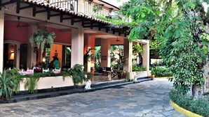 A covered outdoor seating area with tables and chairs, surrounded by greenery and potted plants. - Hôtel du Roi Christophe (Cap-Haitien)