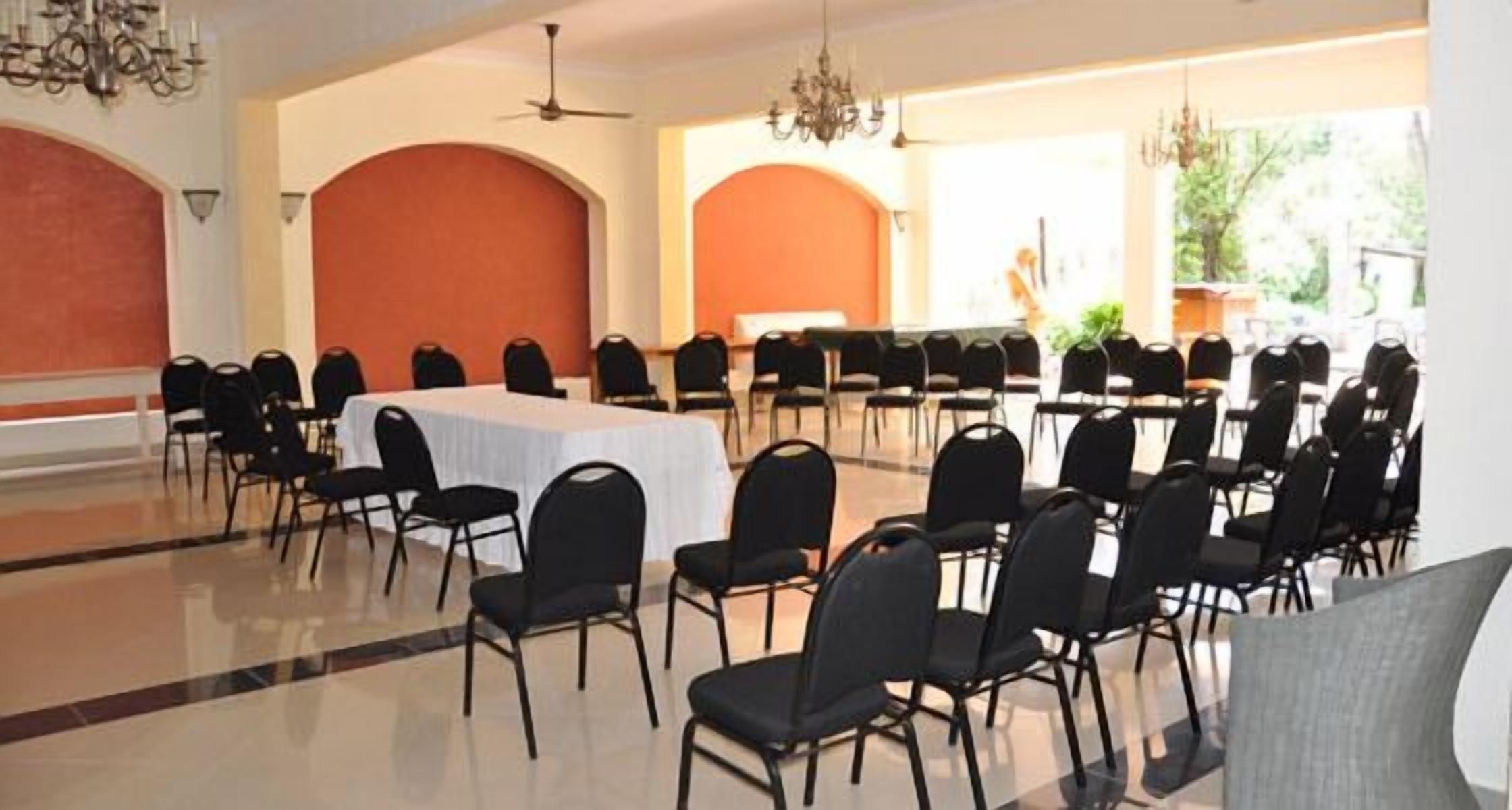 A conference room with a long table and multiple rows of chairs, large windows, and chandeliers.