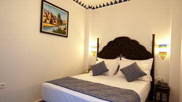 Uma cama bem arrumada com colcha estampada, um quadro na parede e uma luminária decorativa no teto.