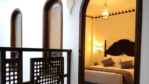 Una habitación de hotel con cama, mesita de noche, lámpara de pared y biombo decorativo.