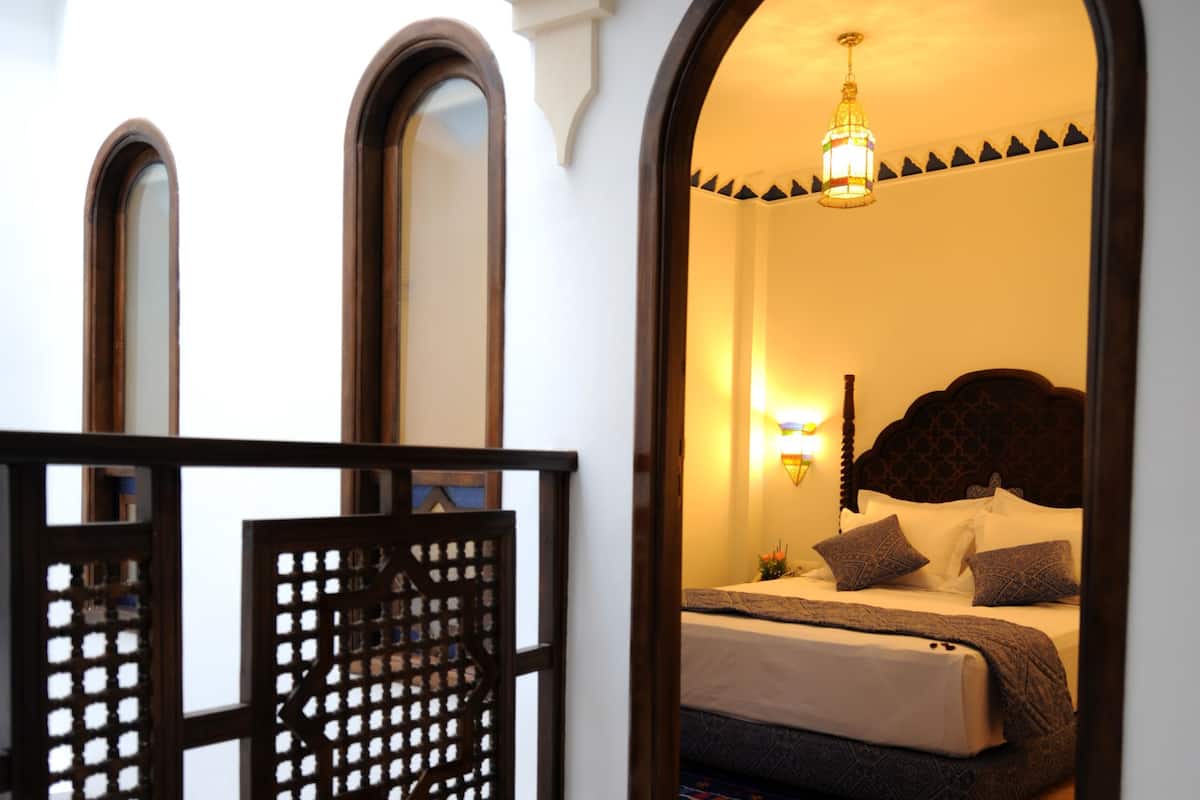 Una habitación de hotel con una cama, una mesita de noche, una lámpara de pared y un separador decorativo.