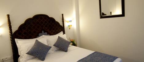 A neatly made bed with a patterned bedspread, a headboard, and two pillows. There is a hanging light fixture above the bed and a mirror on the wall.