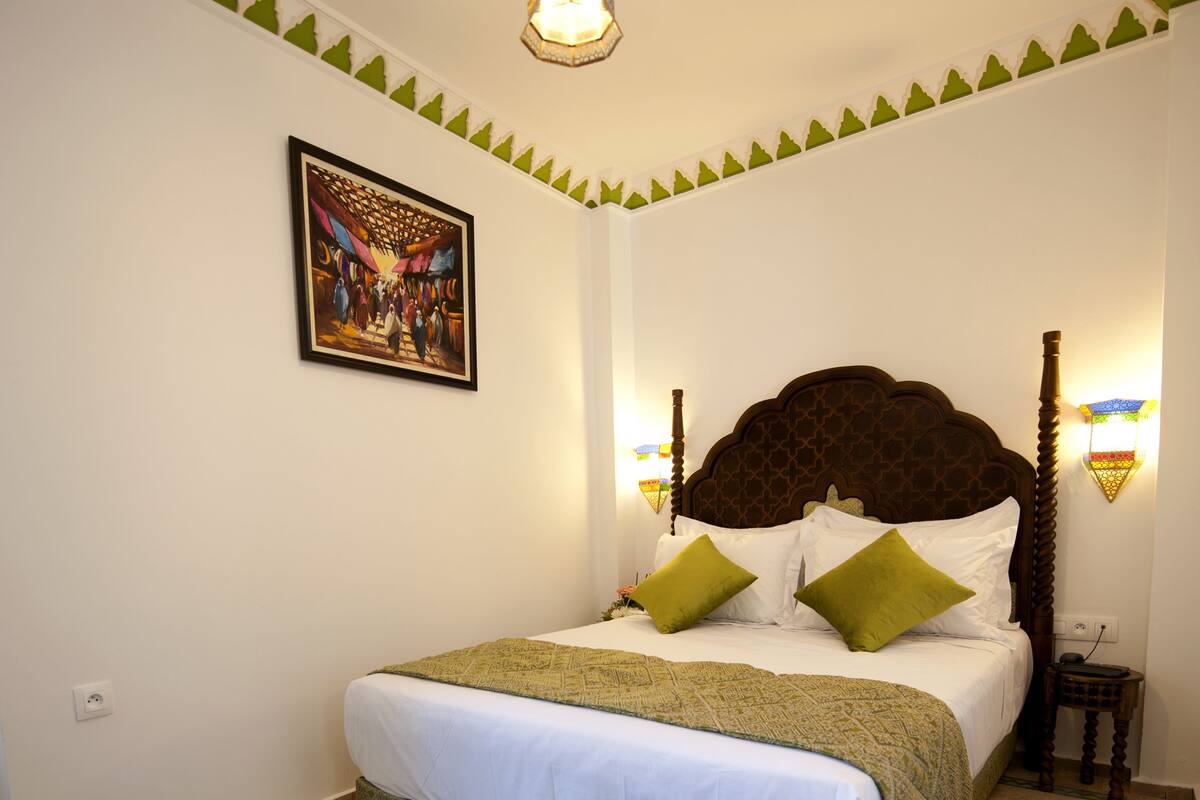Un dormitorio ordenado con una cama grande, un tapete estampado, un adorno de pared y luces fijadas a la pared.