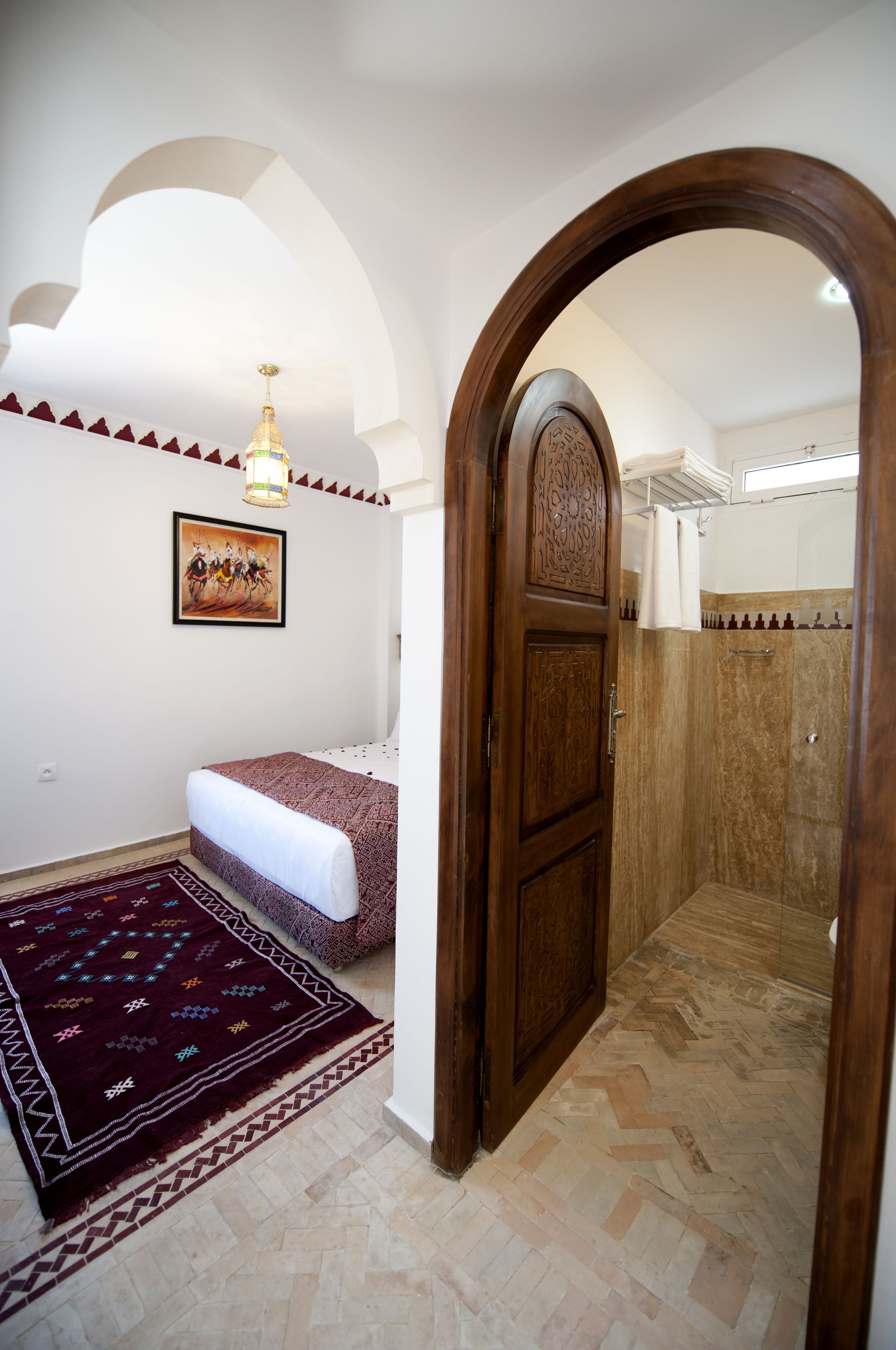 A bedroom with a bed, a rug, a wooden door, and a shower area.