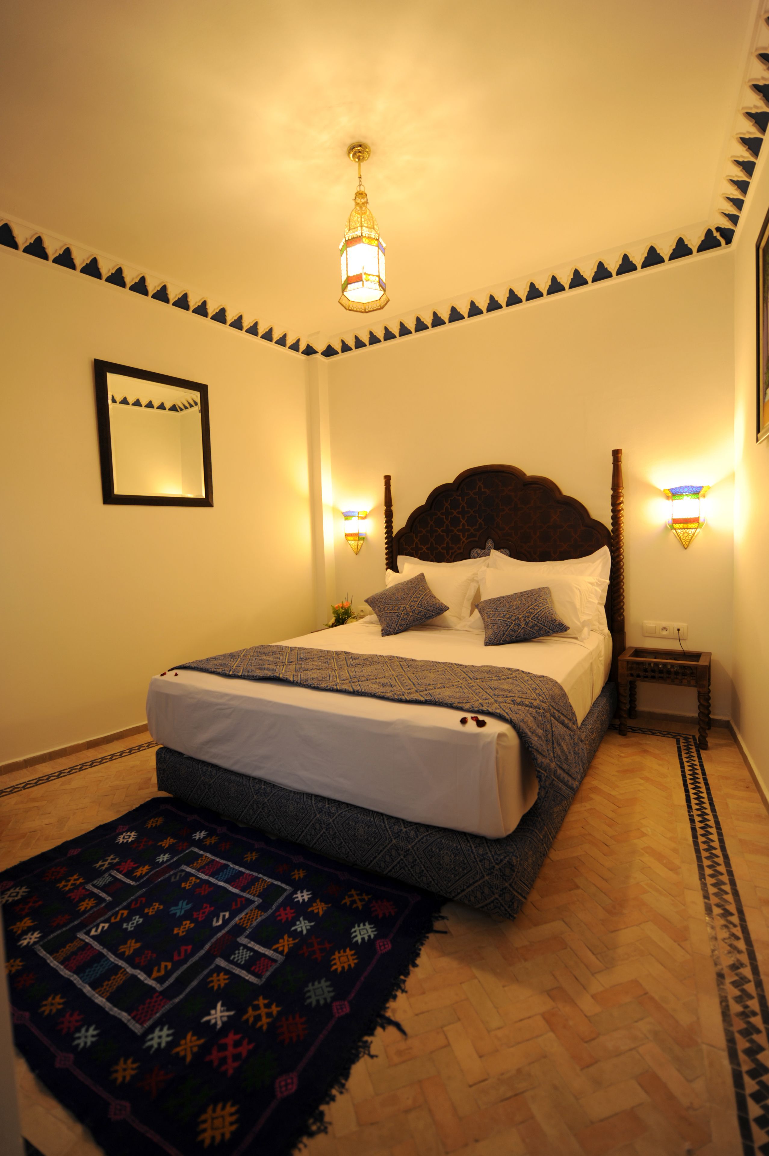 Quarto bem arrumado com cama, abajures, mesa de cabeceira e tapete estampado.