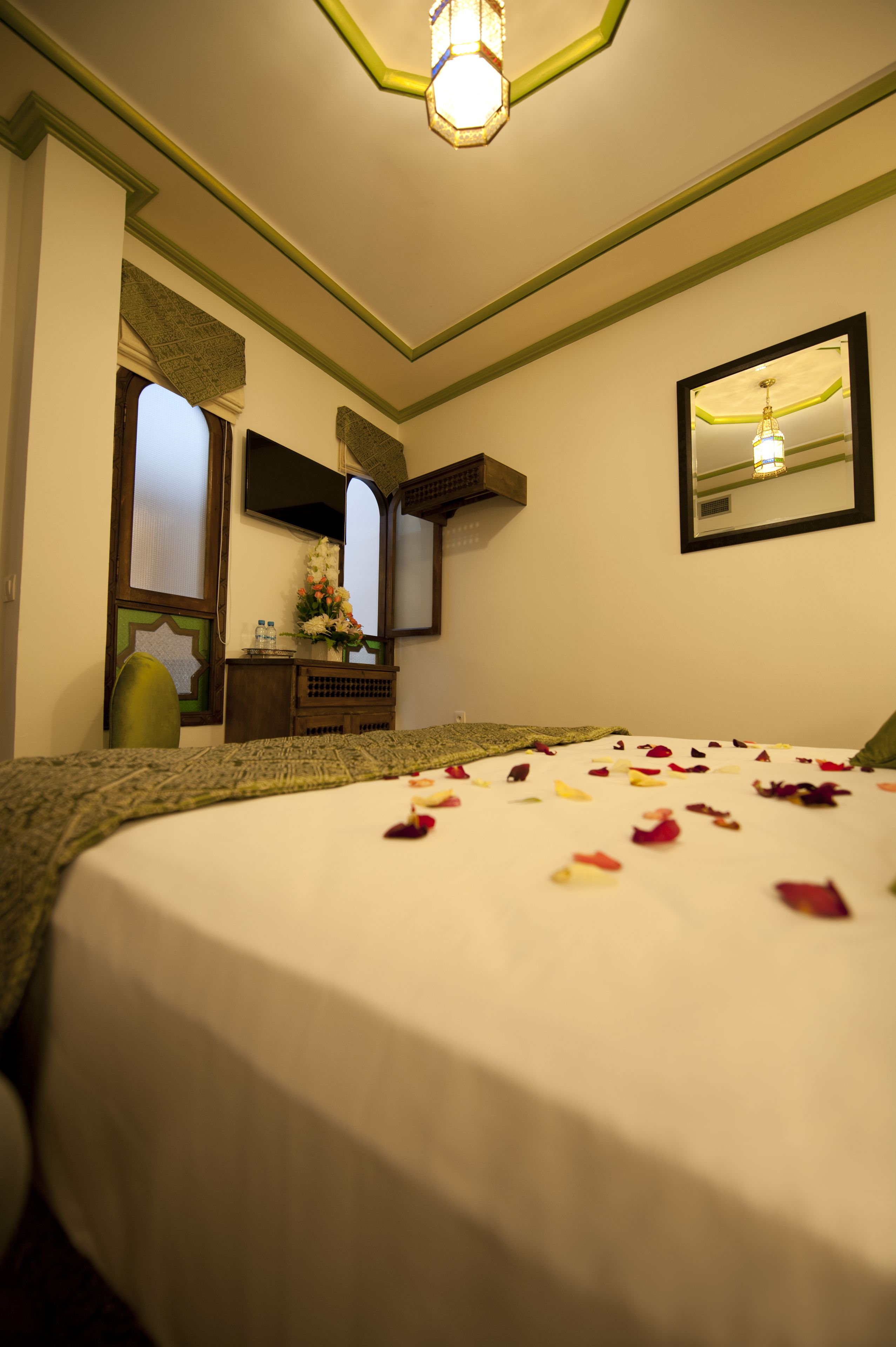 A hotel room with a bed covered in rose petals, a dresser, a mirror, and a green chair.
