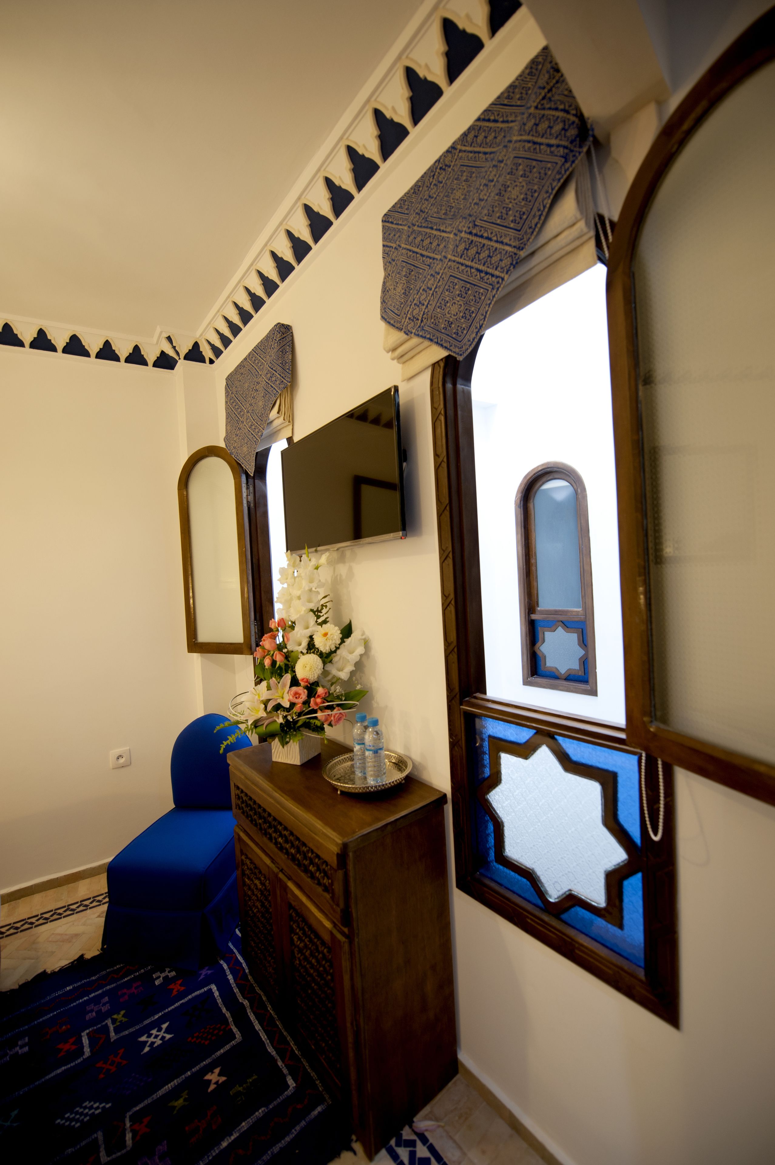 Una habitación con un armario de madera, un espejo, una silla azul y una pared decorativa con patrones geométricos.