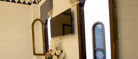 Una habitación con un armario de madera, un espejo, una silla azul y una pared decorativa con patrones geométricos.